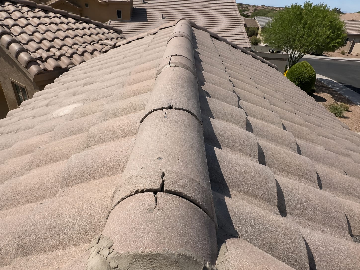 Cracked ridge tiles in three separate locations along the ridge line of a concrete tile roof on an East Valley home in Gilbert, AZ, with mortar patching visible at the lowest crack