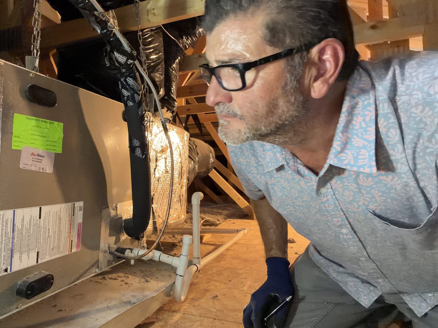 Kelly Lopez examining the air handler and condensate lines of an attic-mounted HVAC system during a Gilbert, AZ home inspection