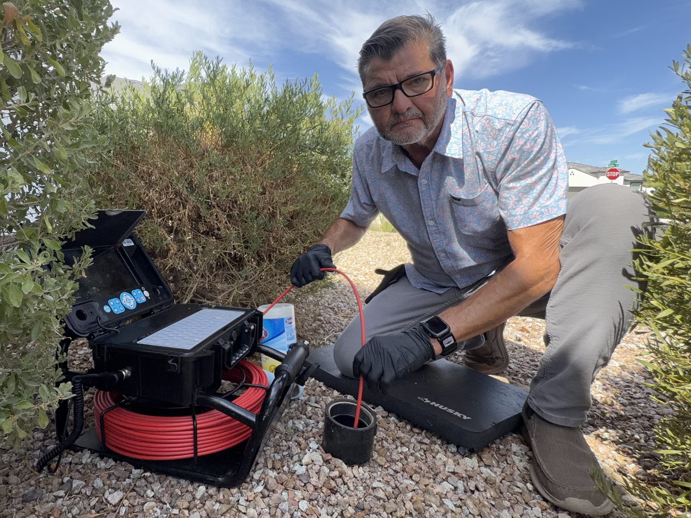 Kelly Lopez feeding a sewer scope camera into the main line cleanout at an East Valley home in Gilbert, AZ